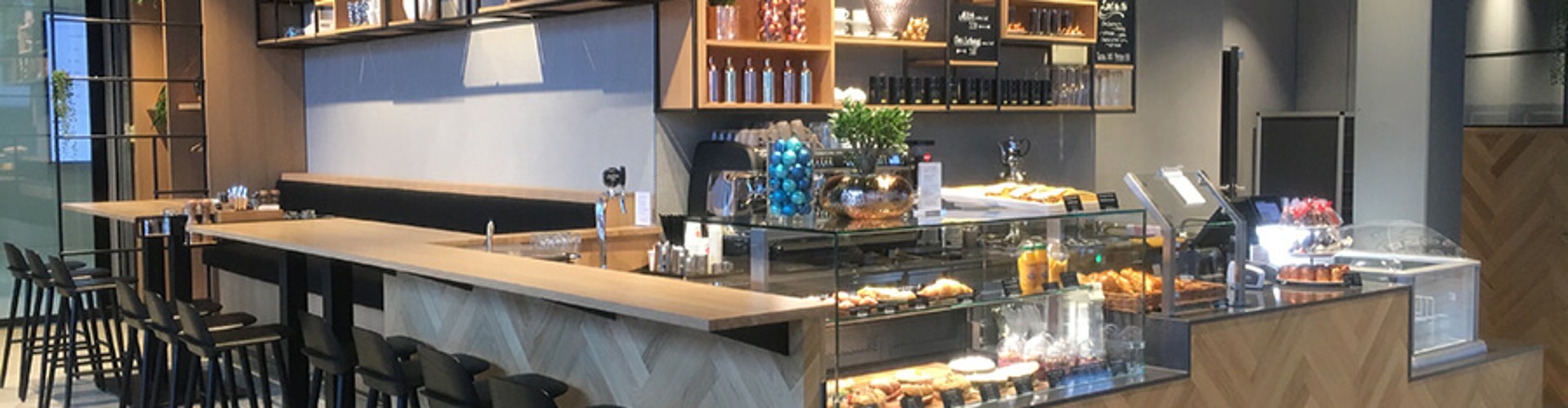 A modern café bar with a display of drinks, pastries, and snacks, featuring stylish lighting and shelves filled with glass containers.