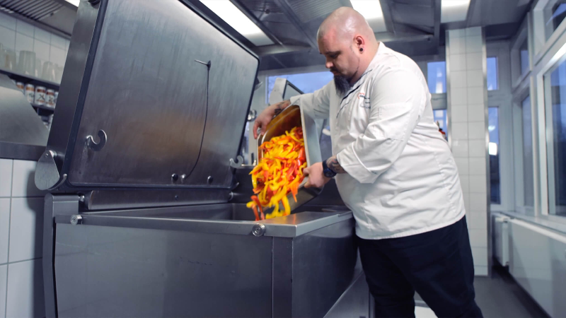 A chef in a professional kitchen tossing sliced vegetables in a large VarioCookingCenter.