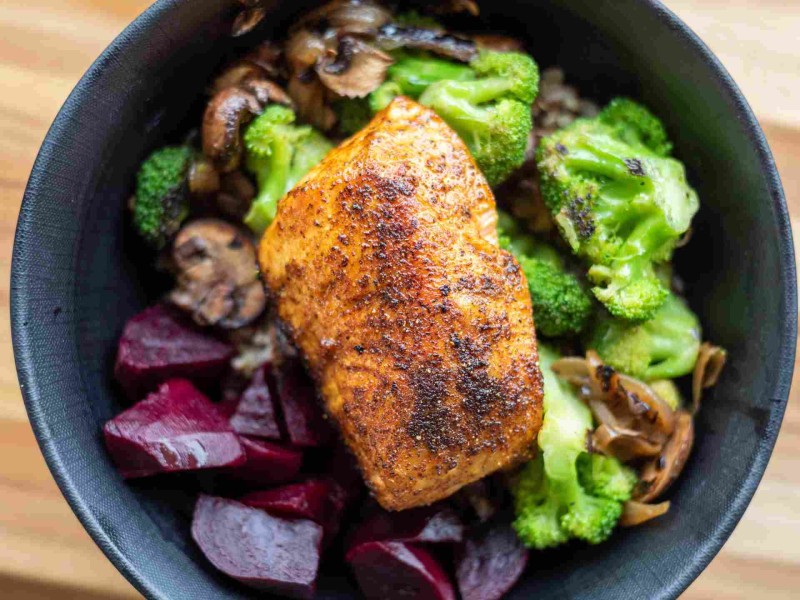 Bowl with grilled salmon, broccoli, mushrooms, and beets over a bed of grains.