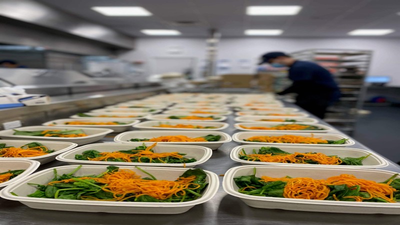 Kitchen scene with multiple containers filled with spinach and shredded carrots, prepared for service.