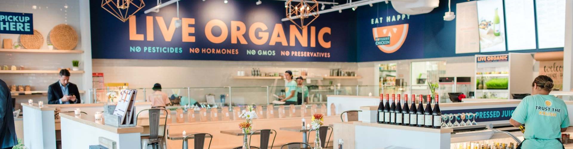 Interior of an organic restaurant featuring a modern design, a display of products, and staff preparing food.