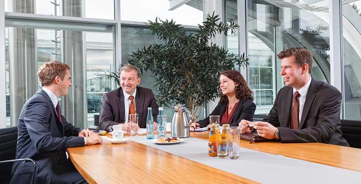 A business meeting with four professionals sitting around a table, engaged in discussion with refreshments.