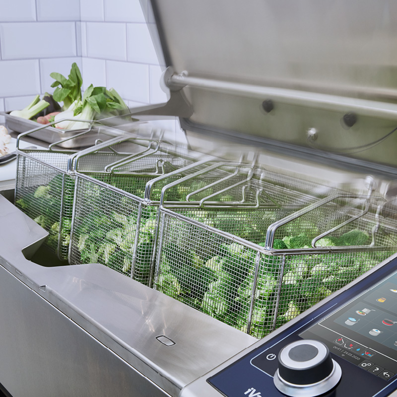 Broccoli cooking in basket inserts inside an open RATIONAL iVario.