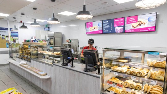 A bakery counter in a supermarket with various baked goods displayed and a staff member assisting customers.