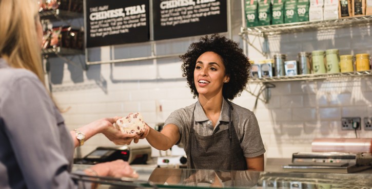 Shop assistant behind counter handing bread to customer.