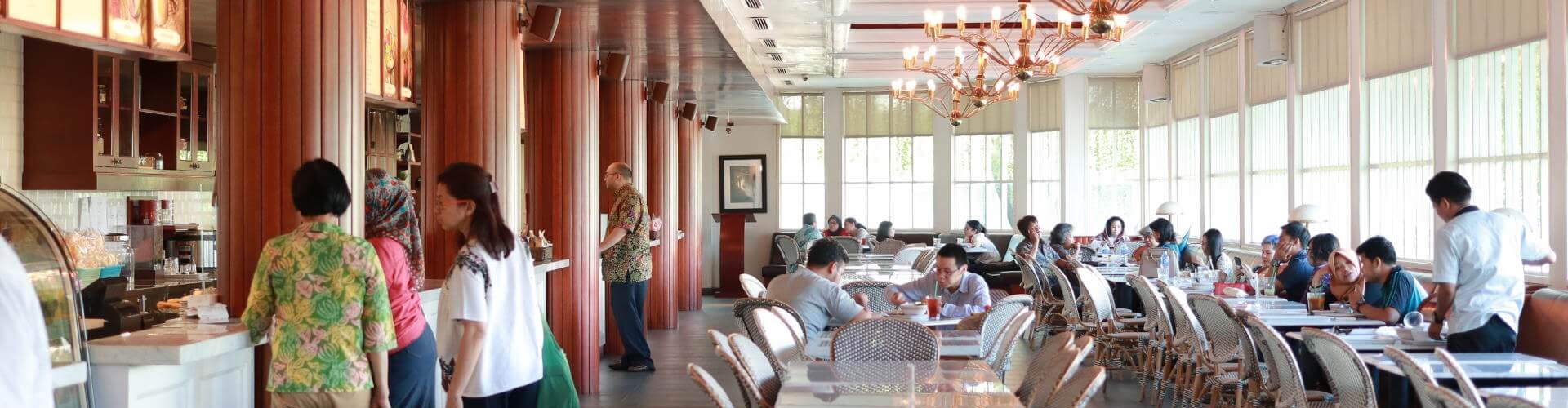 A spacious dining area with people at the counter and seated at tables, featuring elegant lighting and modern decor.