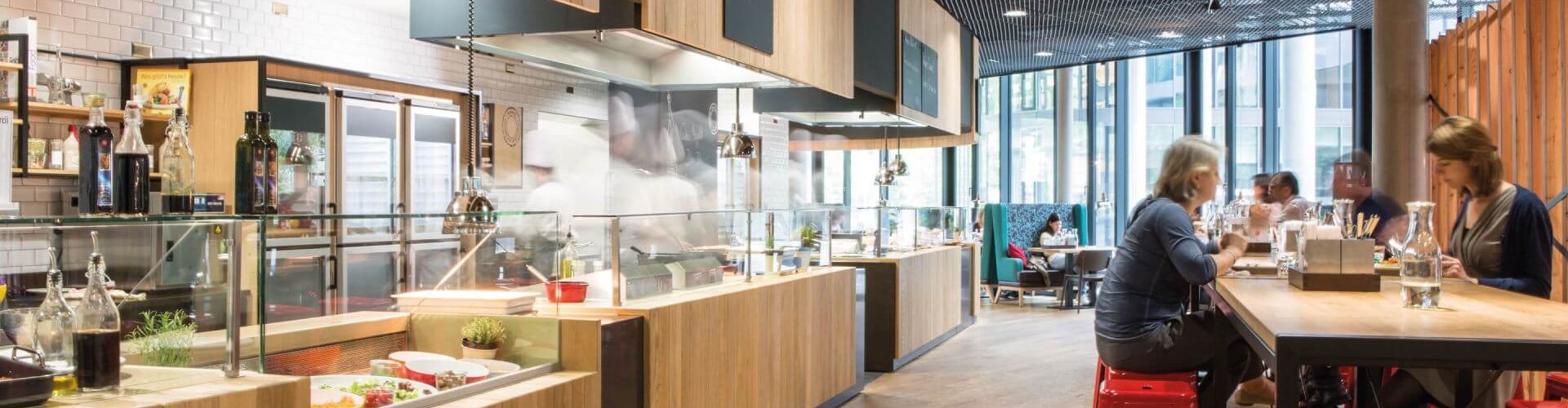 A casual dining space featuring a salad bar, wooden counters, and red stools, with patrons enjoying their meals in a modern setting.