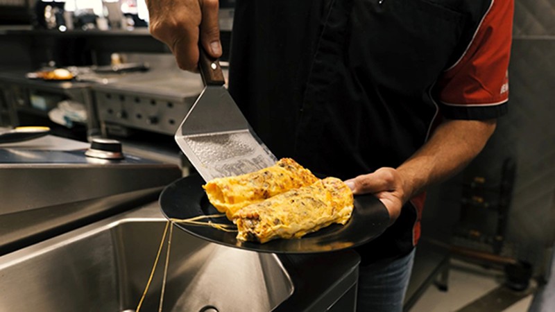 A chef uses a spatula to serve a freshly cooked omelette on a plate in a kitchen.