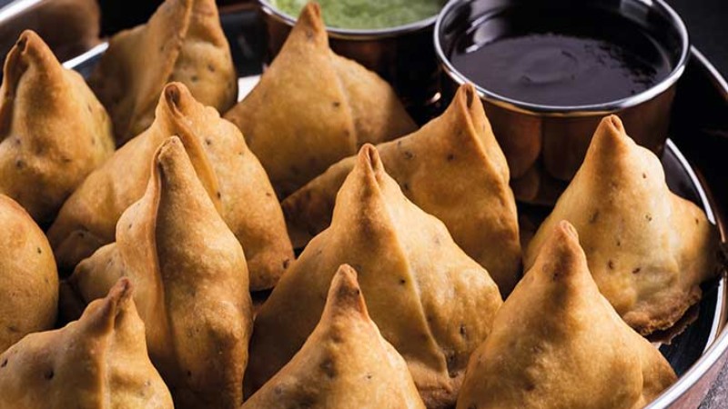 A platter of golden-brown samosas arranged neatly, served with green chutney and tamarind sauce in small bowls.