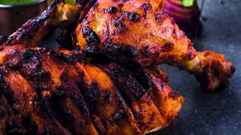 A close-up of grilled tandoori chicken, served with fresh herbs and garnishes.