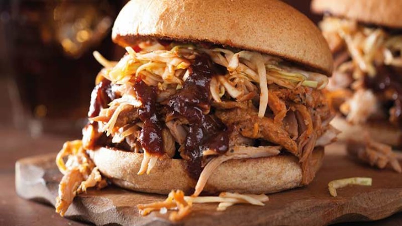 A delicious pulled pork sandwich piled high with coleslaw and barbecue sauce, served on a whole grain bun.