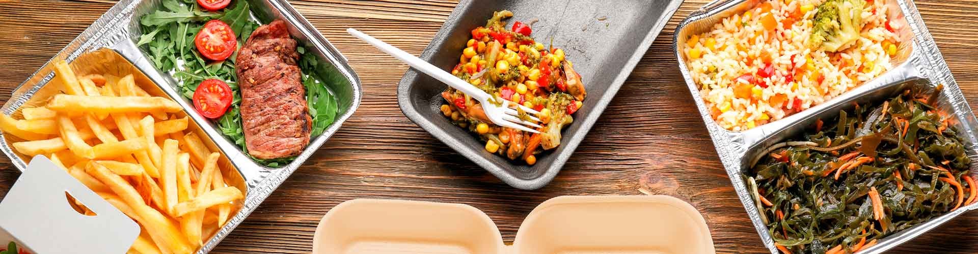 A variety of takeaway food in different containers, including fries, steak, vegetables, rice, and salad on a wooden table.