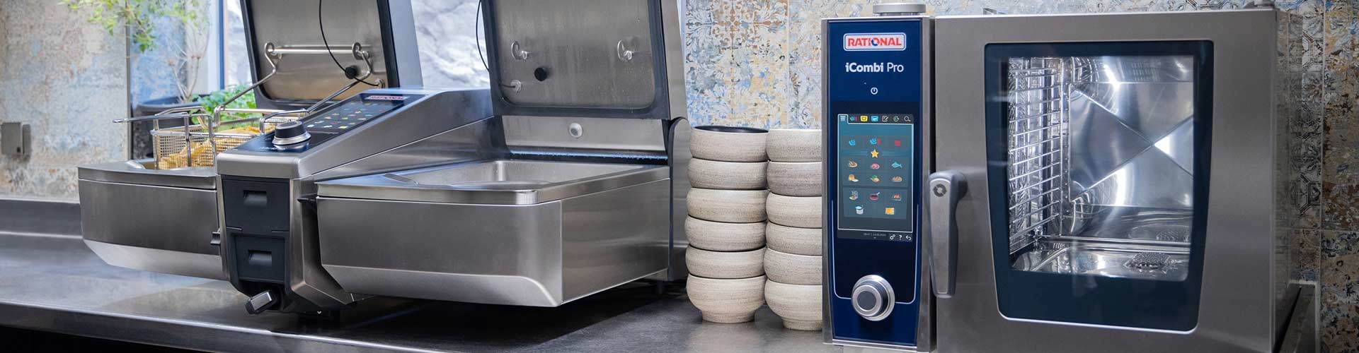 A view of a Rational iCombi Pro oven next to an iVario cooking appliance, both in a modern kitchen setting with stacked bowls in the background.
