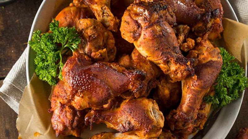 A platter of smoked chicken legs, beautifully browned and garnished with fresh parsley, served on parchment paper.