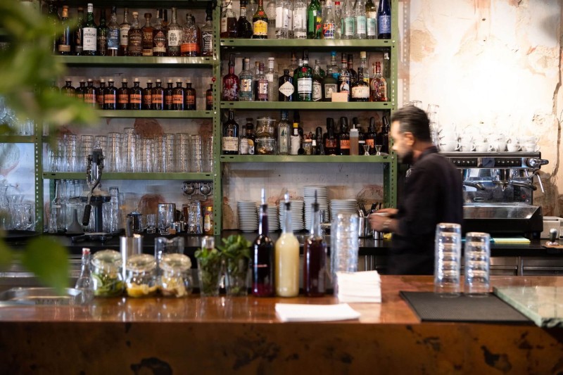 A busy bar scene with shelves filled with various liquor bottles, glasses, and a bartender preparing drinks.