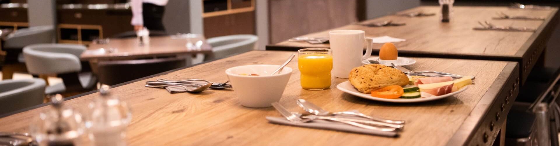 A wooden dining table set for breakfast with a variety of foods, including a plate with bread, fruit, and a cup of juice.