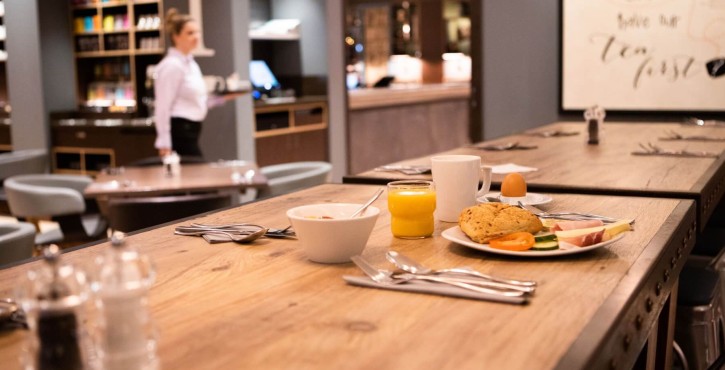 A wooden dining table set for breakfast with a variety of foods, including a plate with bread, fruit, and a cup of juice.
