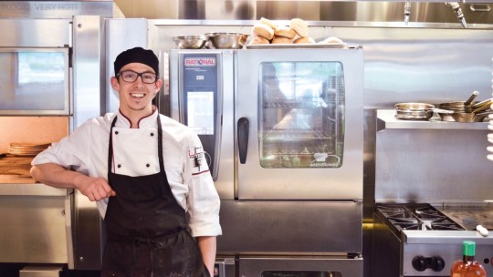 Smiling chef in a professional kitchen in front of a Rational iCombi combi-steamer.