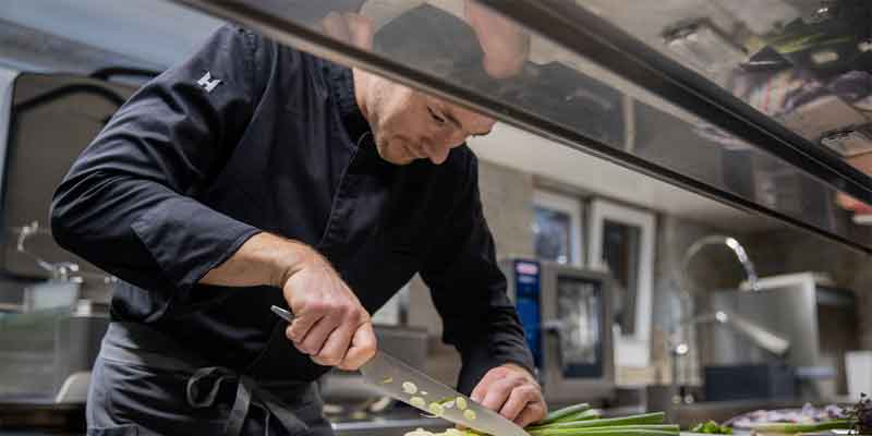 Chef slicing spring onions in a professional kitchen.