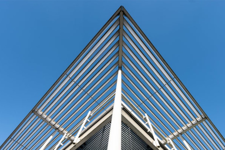 Structure architecturale moderne avec poutres en acier formant un toit triangulaire sous ciel bleu clair.