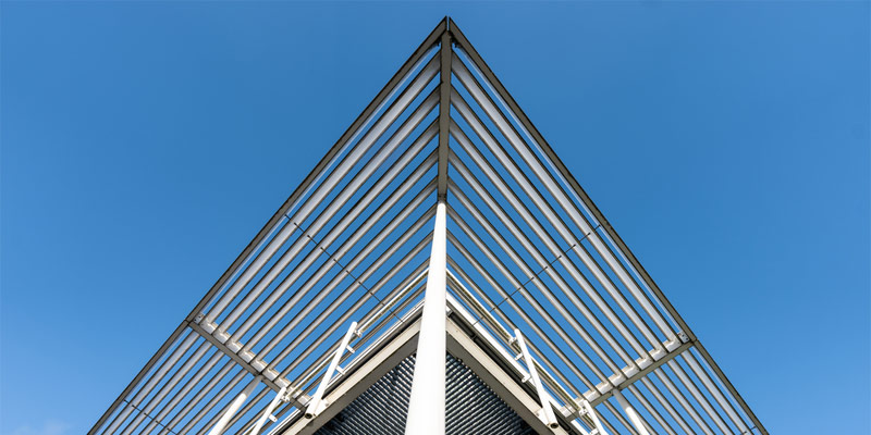 Estructura arquitectónica moderna con vigas de acero formando un techo triangular bajo un cielo despejado.