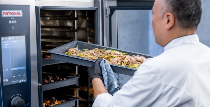 工作人员将装有熟食与配菜的烤盘放入RATIONAL 膳酷 混合蒸锅，展示多层烹饪功能。