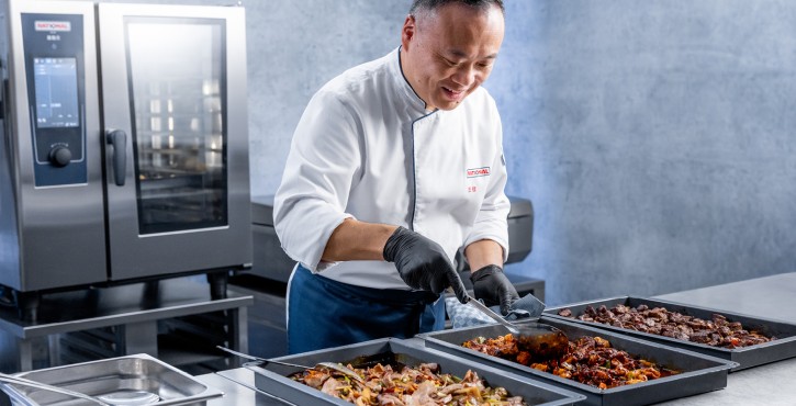 工作人员在不锈钢操作台前分装多盘熟食，背景可见RATIONAL 膳酷 混合蒸锅。