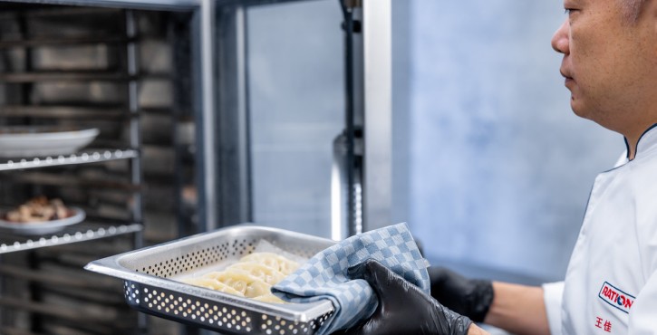 工作人员将盛有蒸制食材的打孔烤盘放入RATIONAL 膳酷 混合蒸锅，展示设备蒸制功能。