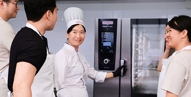 多位学员在厨房围绕RATIONAL iCombi Pro 混合蒸锅学习操作，厨师示范开启设备门。
