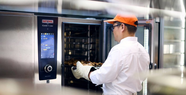 工作人员将烤制食材推入RATIONAL iCombi Pro 混合蒸锅，设备显示屏清晰呈现烹饪信息。