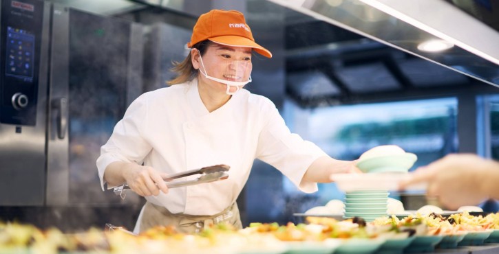 工作人员在餐台前分发餐盘，旁侧可见RATIONAL iCombi Pro 混合蒸锅运行中的界面。