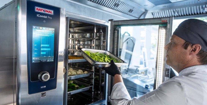 工作人员将盛有绿叶蔬菜的烤盘推入RATIONAL iCombi Pro 混合蒸锅，设备内多层烤架清晰可见。